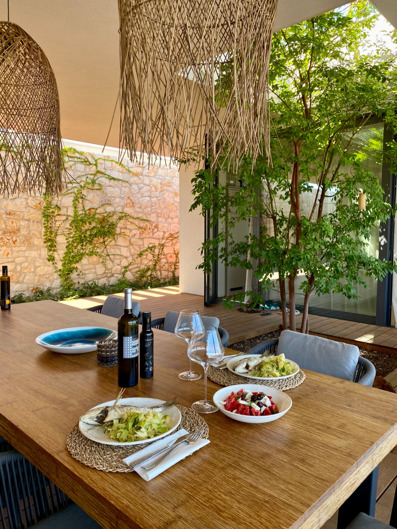 Outdoor dining table set with local wine, olive oil and fresh fish under woven pendants